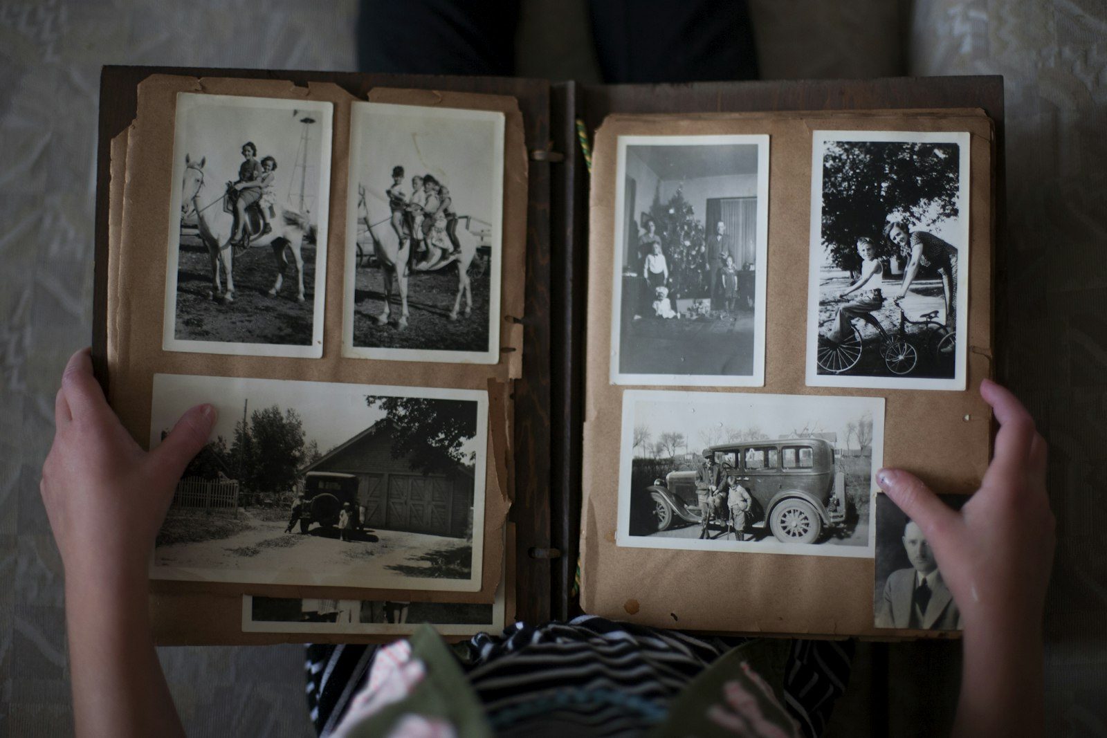 Mains tenant un album photo familial sépia ouvert, avec des photographies d'enfance, voitures anciennes, scènes de famille